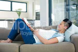 Pregnant woman reading a book while lying on sofa