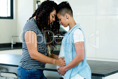 Pregnant lesbian couple embracing in kitchen