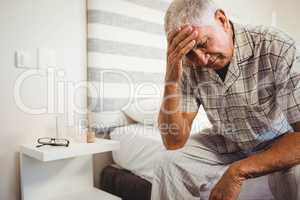 Frustrated senior man sitting on bed