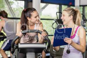 Trainer woman talking with a woman doing exercise bike