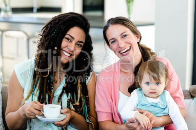 Portrait of two women sitting on sofa with a baby