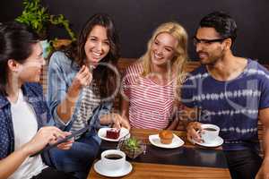 Smiling friends enjoying coffee together and using technologies
