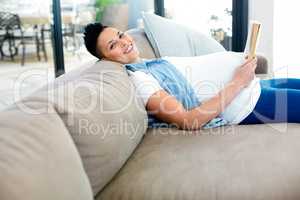 Portrait of pregnant woman reading a book while lying on sofa