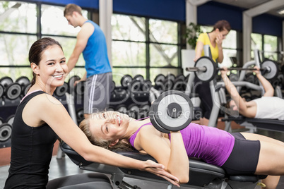 Smiling woman working out with dumbbells with female trainer