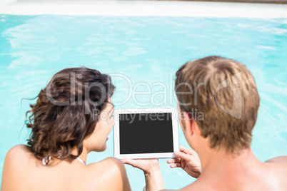 Young couple looking at digital tablet by poolside