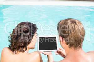 Young couple looking at digital tablet by poolside