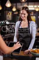 Smiling barista looking at tablet while woman is ordering