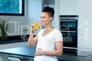 Pregnant woman drinking juice in kitchen