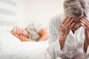 Frustrated senior woman sitting on bed