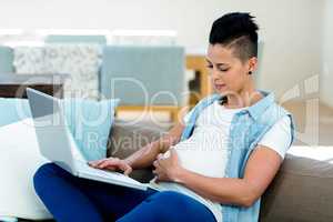 Pregnant woman relaxing on sofa with her laptop