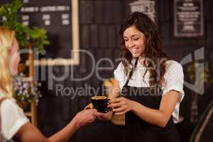Pretty waitress offering cup of coffee to customer