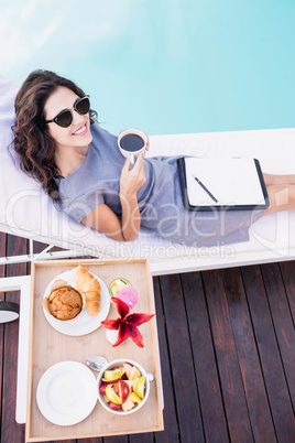 Young woman having cup of tea near poolside