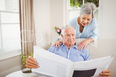 Senior woman talking to senior man reading newspaper