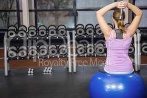 Determined woman lifting dumbbell on fitness ball