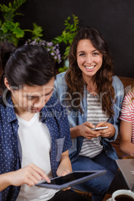 Smiling friends enjoying coffee together and using technologies