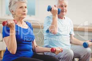 Senior couple sitting on fitness balls with dumbbells