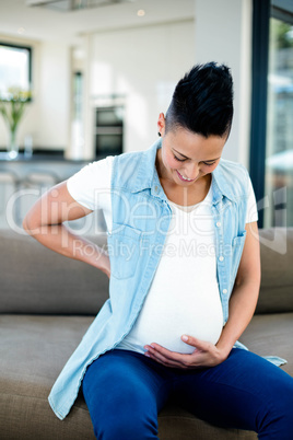 Pregnant woman sitting on sofa with and on stomach