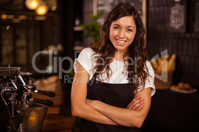 Pretty waitress posing with arms crossed next to coffee machine