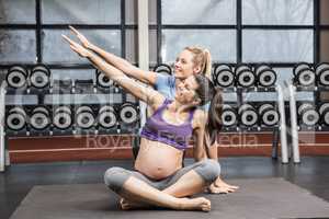 Smiling trainer and pregnant woman overstretching arm