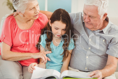 Grandparents reading a book with granddaughter