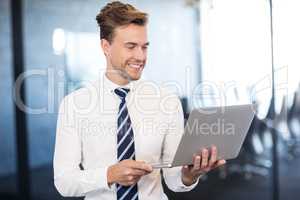 Portrait of businessman standing with a laptop in office