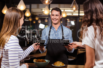Smiling barista giving coffees to women