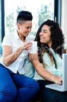 Happy lesbian couple having coffee and using laptop