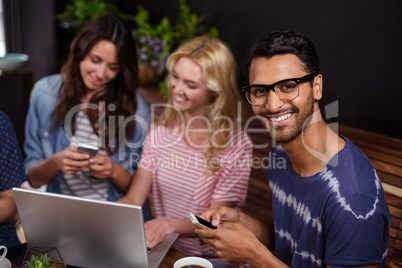 Smiling friends enjoying coffee together and using technologies