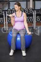 Determined woman lifting dumbbells on fitness ball