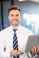 Portrait of businessman standing with a laptop in office