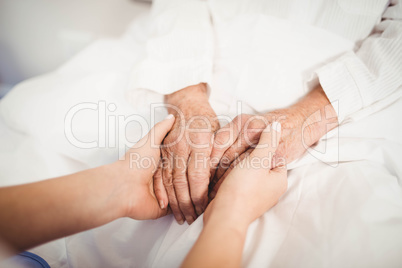 Senior woman and nurse holding hands