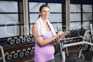 Smiling pregnant woman writing on clipboard