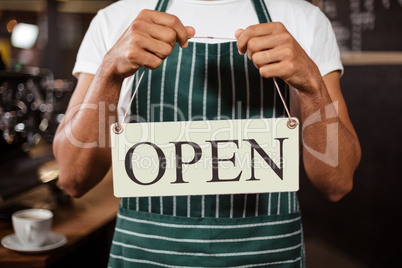 Mid section of barista holding open sign