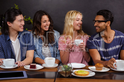 Smiling friends enjoying coffee together and using technologies