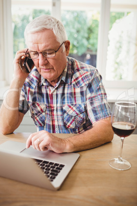 Worried senior man taking on phone while using laptop