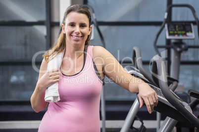 Smiling pregnant woman standing next to exercise bike