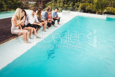 Young people sitting by swimming pool