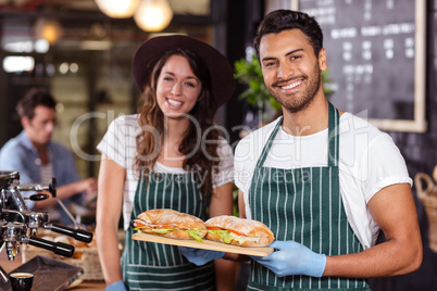 Smiling baristas holding sandwiches