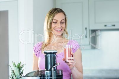 Blonde woman holding a smoothie glass in the kitchen