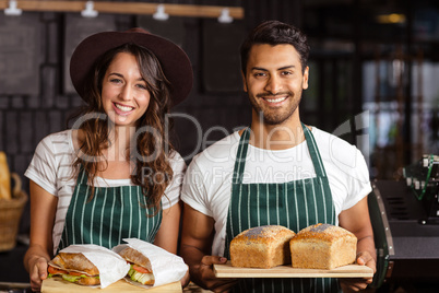 Smiling baristas holding bread and sandwiches