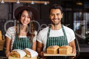 Smiling baristas holding bread and sandwiches