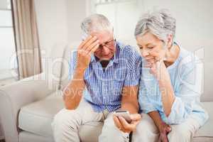 Sad senior couple looking at mobile phone