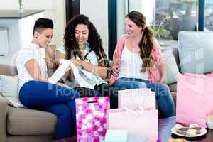 Three women sitting on sofa and looking at babys clothes