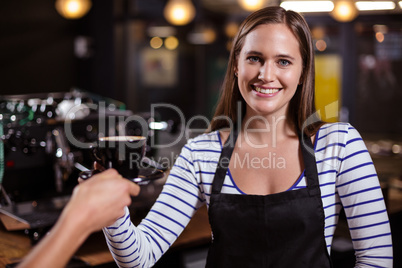 Pretty barista giving coffee to customer and smiling at the came