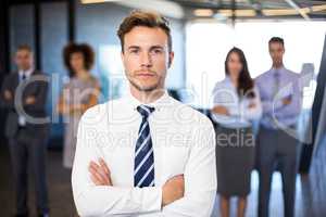 Businessman smiling at camera while his colleagues standing in b