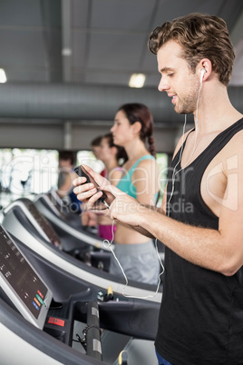 Smiling muscular man on treadmill listening to music