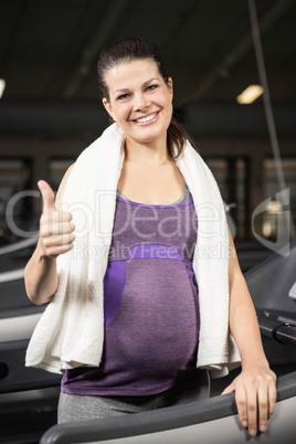 Smiling pregnant woman standing on treadmill showing thumb up