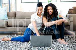 Smiling lesbian couple sitting on rug and using laptop