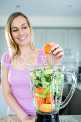 Blonde woman preparing a smoothie in the kitchen