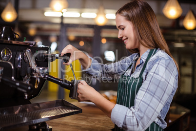 Smiling barista making hot milk with coffee machine